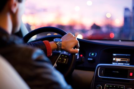 Motorista TVDE ao volante, cidade ao entardecer